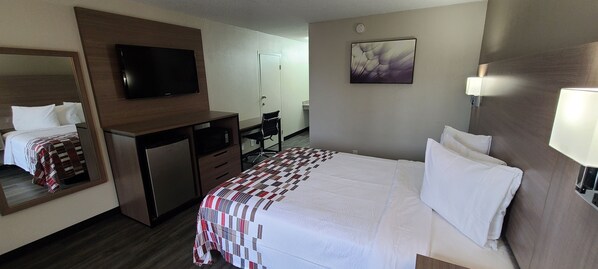 Una habitación de hotel con una cama, un escritorio, una silla, un televisor y un cuadro en la pared.
