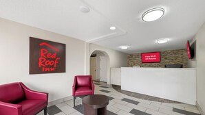 Un hall d’entrée d’un hôtel Red Roof Inn, avec un comptoir d’accueil, deux fauteuils rouges et une petite table.