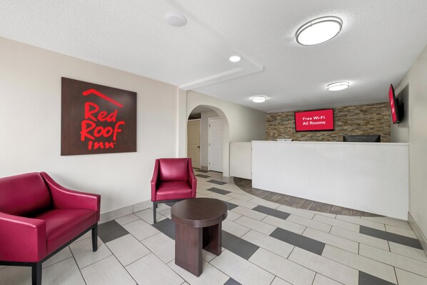 Un hall d’entrée d’un hôtel Red Roof Inn, avec un comptoir d’accueil, deux fauteuils rouges et une petite table.
