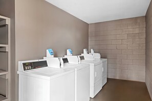 A laundry room with four white washing machines and dryers, a control panel, and a brick wall. - Red Roof Inn Charlotte - Airport (Charlotte)