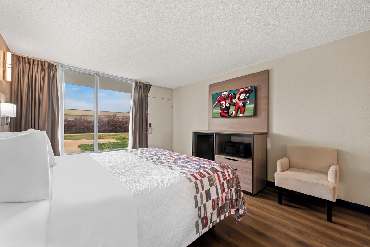 A hotel room with a large bed, a TV mounted on the wall, a chair, and a view of the outdoors.