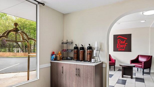 Un espace d’accueil d’hôtel avec un comptoir en bois, des machines à café et une enseigne « Red Roof ».