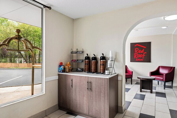 Un espace d’accueil d’hôtel avec un comptoir en bois, des machines à café et une enseigne « Red Roof ».