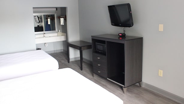 A hotel room with a bed, a desk, a television, and a mirror. - River Front Inn (Conway)