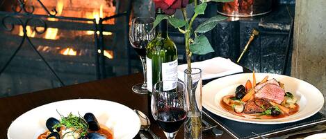 A dining table with two plates of food, a bottle of wine, a glass of wine, and a rose.