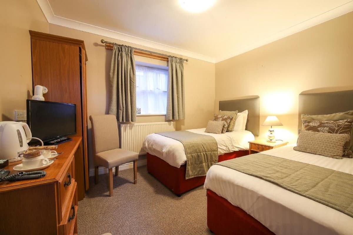 A hotel room with a bed, a desk with a TV, a chair, and a window with curtains.
