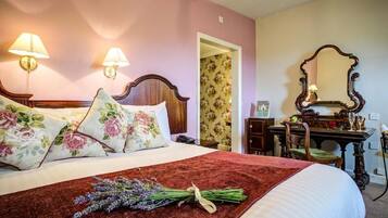 Una cama bien hecha con almohadas florales, una manta roja y un ramo de lavanda.