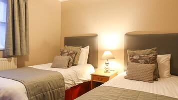 A hotel room with two beds, each with a headboard, a bedside table with a lamp, and a window with curtains.
