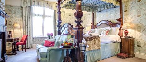 A four-poster bed with a canopy, a sitting area with a chair and a table, and a small side table with a lamp.