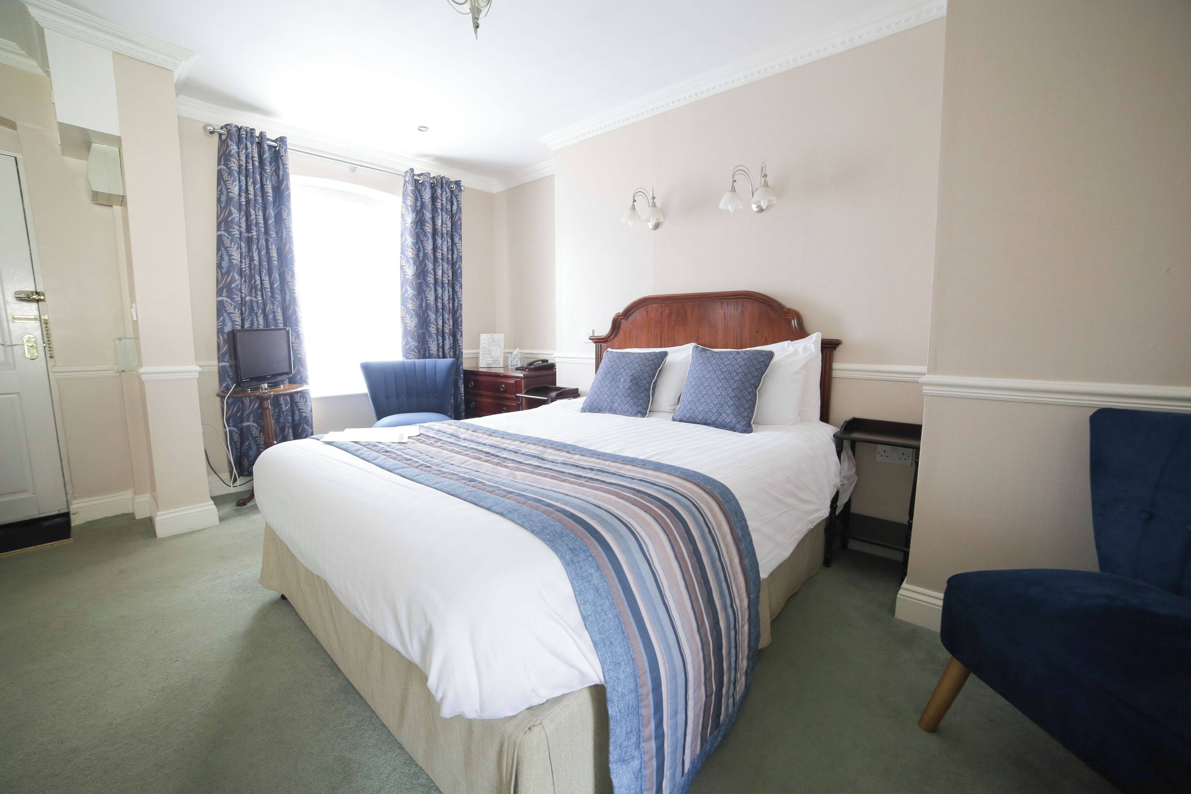 A hotel room with a large bed, a television, a desk, and a chair.