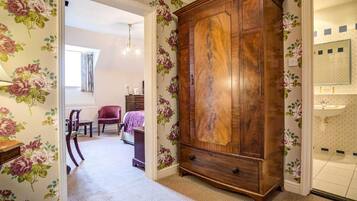Un dormitorio con papel tapiz floral, un armario de madera, una cama y un baño con espejo y lavamanos.