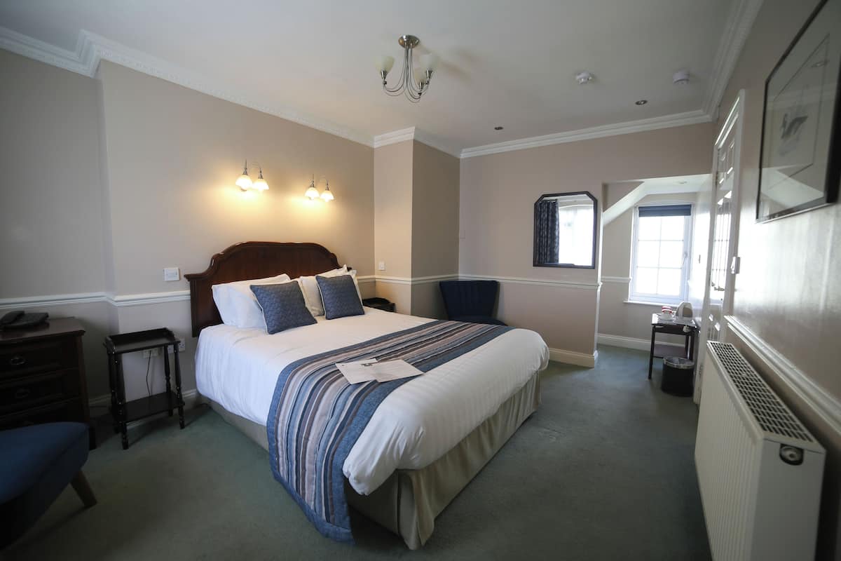 A bedroom with a large bed, a nightstand, a dresser, and a chair. There is a window with a view of the outside.