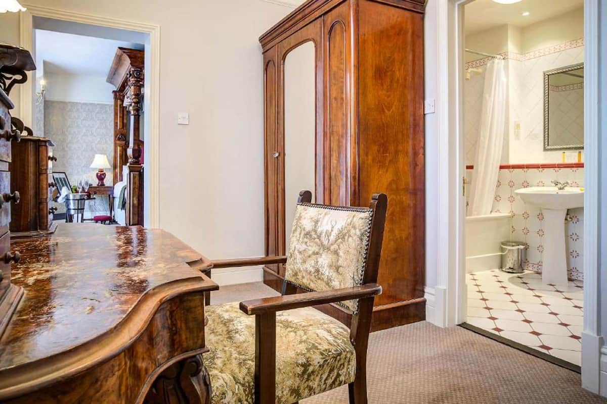 A dining area with a wooden table and chairs, a large wooden cabinet, and a bathroom with a tiled floor and a sink.