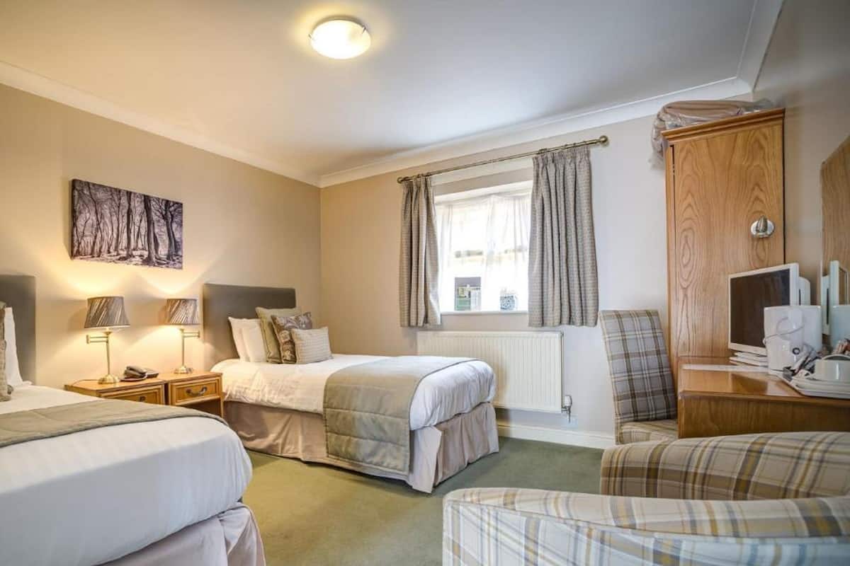 A hotel room with two beds, a desk with a computer, a chair, and a window with curtains.