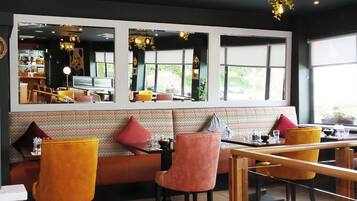 Un restaurante con una decoración moderna, que cuenta con una barra larga, varias zonas de estar con sillas acolchadas y amplios ventanales que permiten la entrada de luz natural.