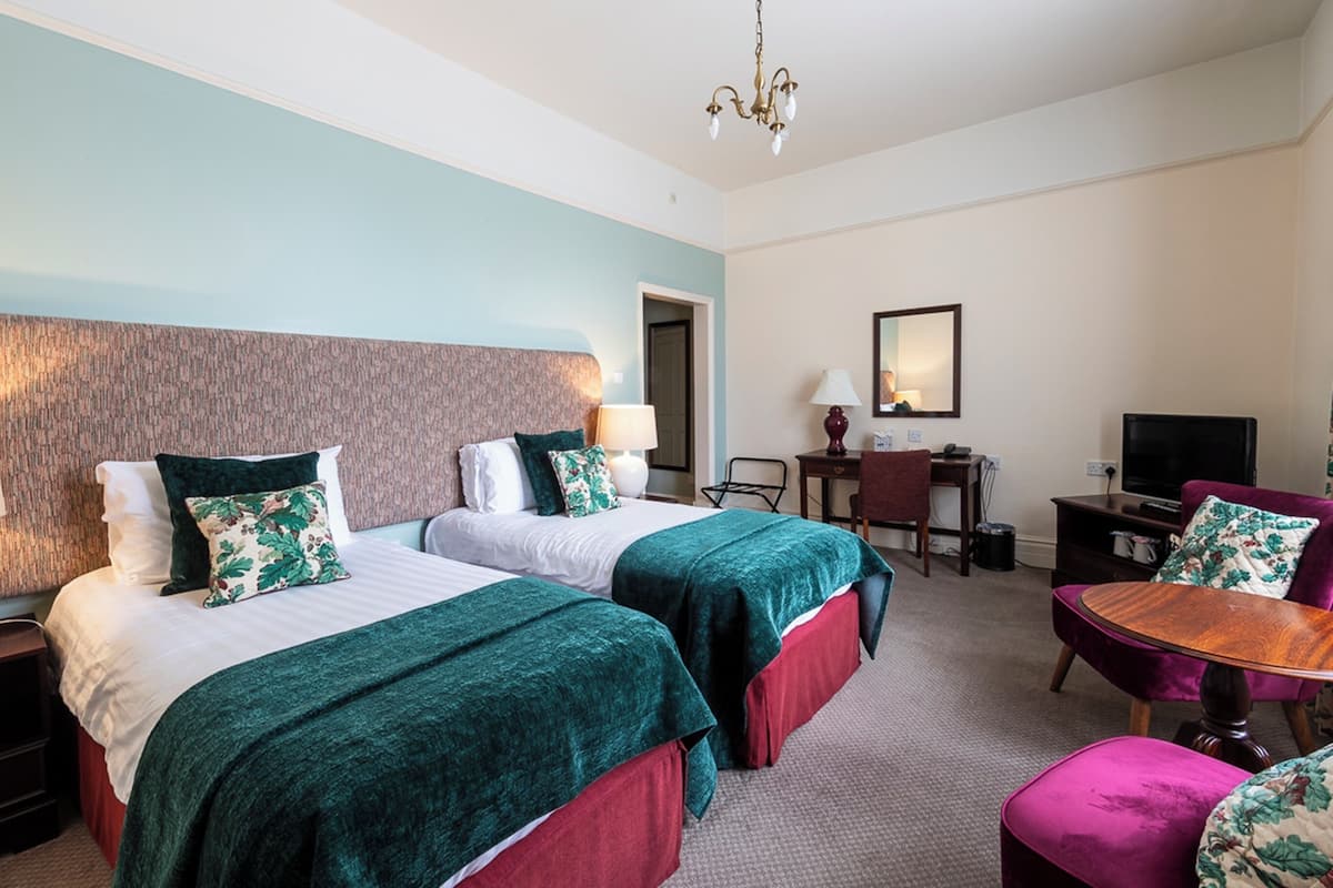 A hotel room with two beds, a desk, a chair, and a TV.