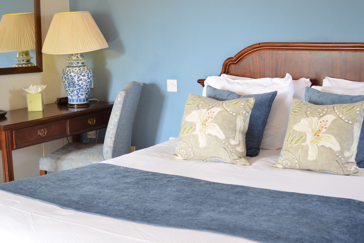 A neatly made bed with floral pillows, a blue throw blanket, and a wooden headboard.