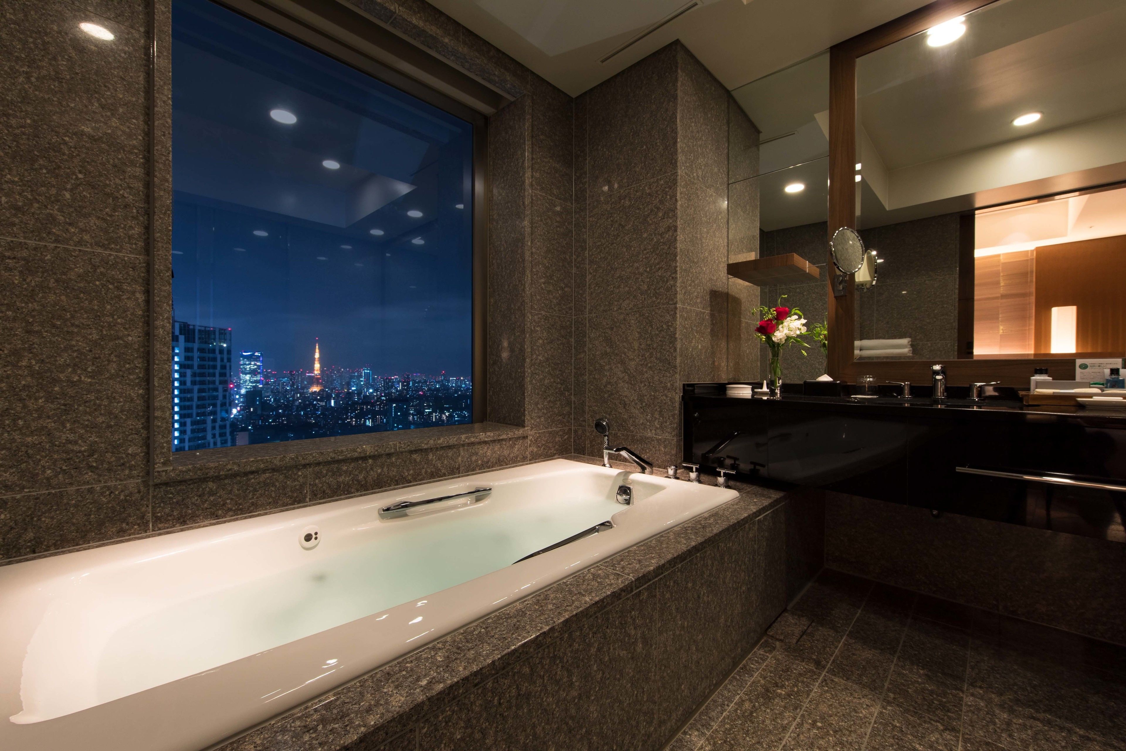 Un baño moderno con una bañera grande, un tocador con espejo y vistas a un paisaje urbano nocturno.