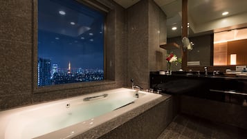 Un baño moderno con una bañera grande, un tocador con espejo y vistas a un paisaje urbano nocturno.