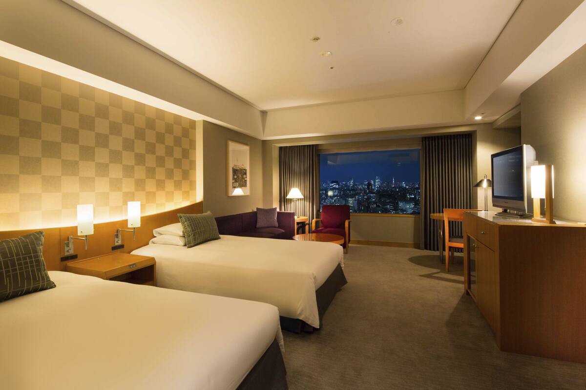 A hotel room with two beds, a desk, a chair, and a TV.