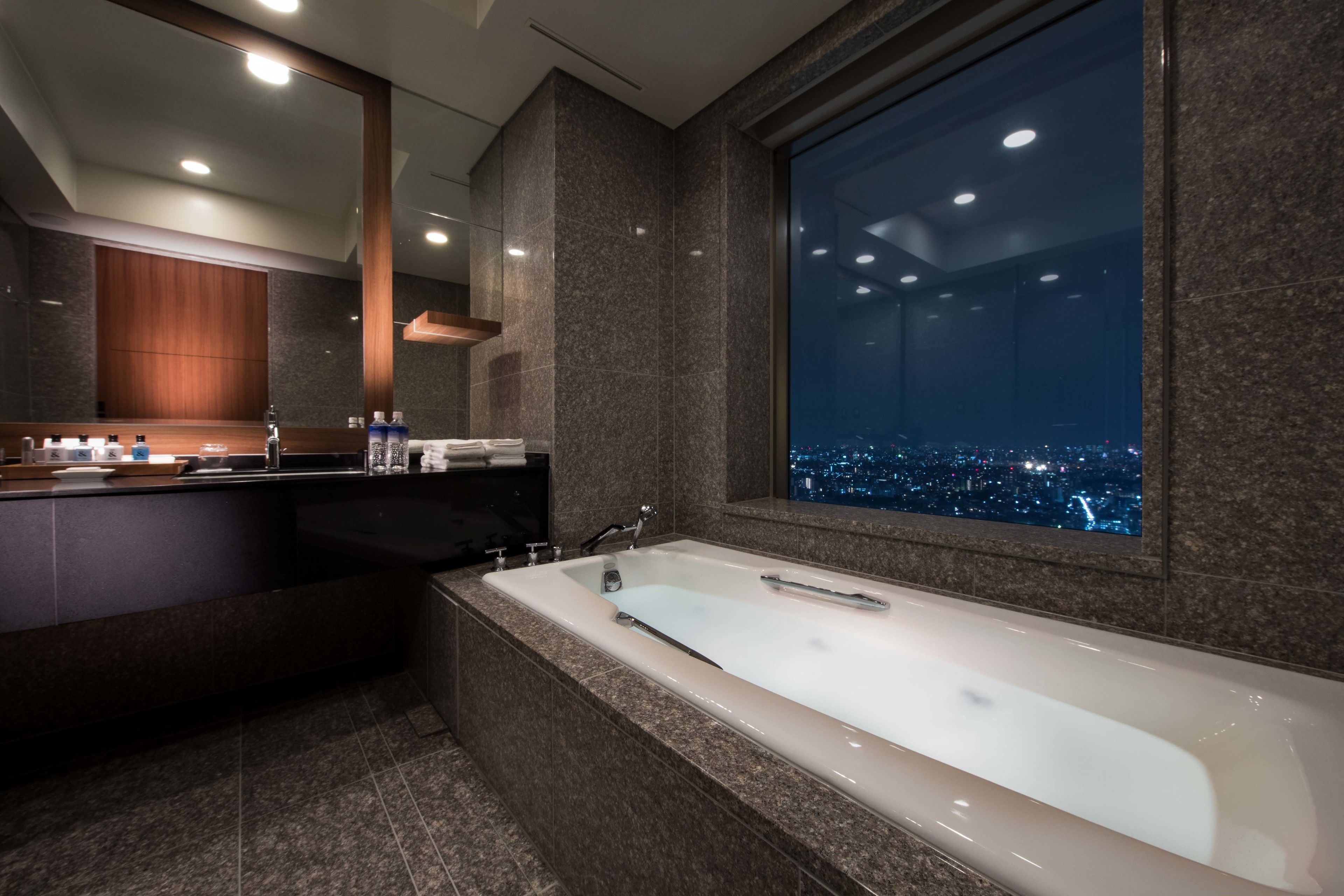 Ein modernes Badezimmer mit einer großen Badewanne, einem Waschtisch mit Spiegel und Blick auf die Stadt durch ein großes Fenster.