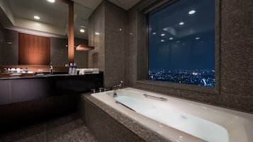 Ein modernes Badezimmer mit einer großen Badewanne, einem Waschtisch mit Spiegel und Blick auf die Stadt durch ein großes Fenster.