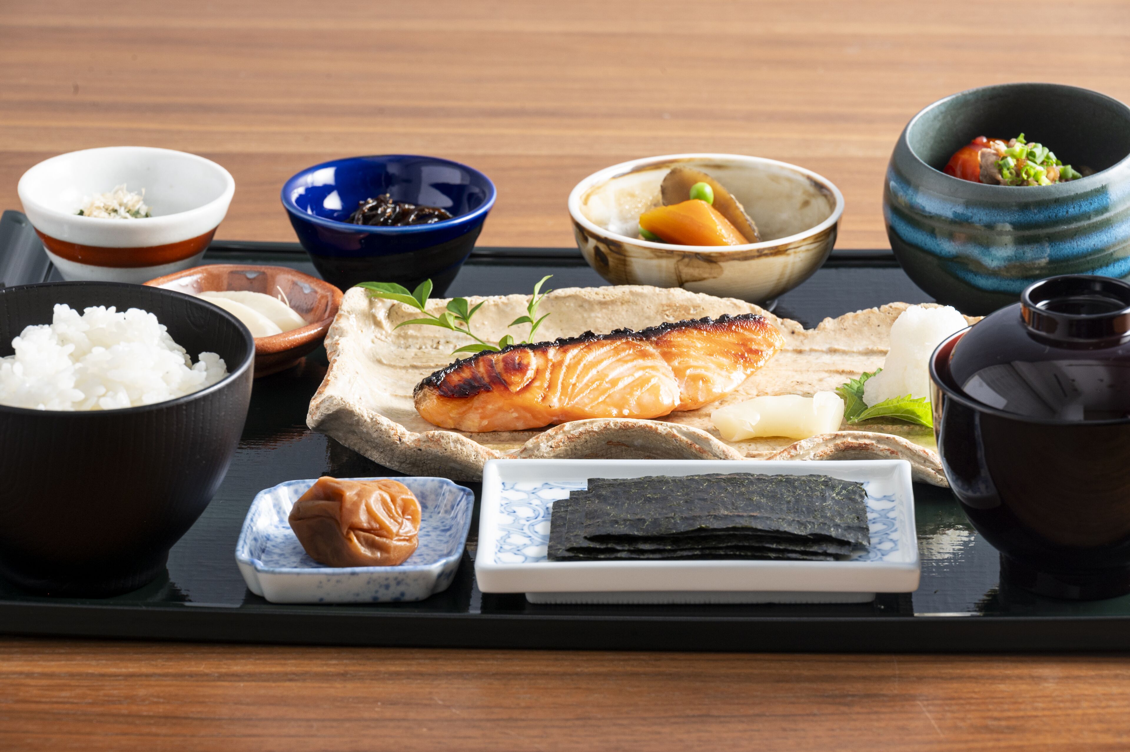 Una bandeja con diversos platos japoneses, incluyendo salmón, arroz y algas.