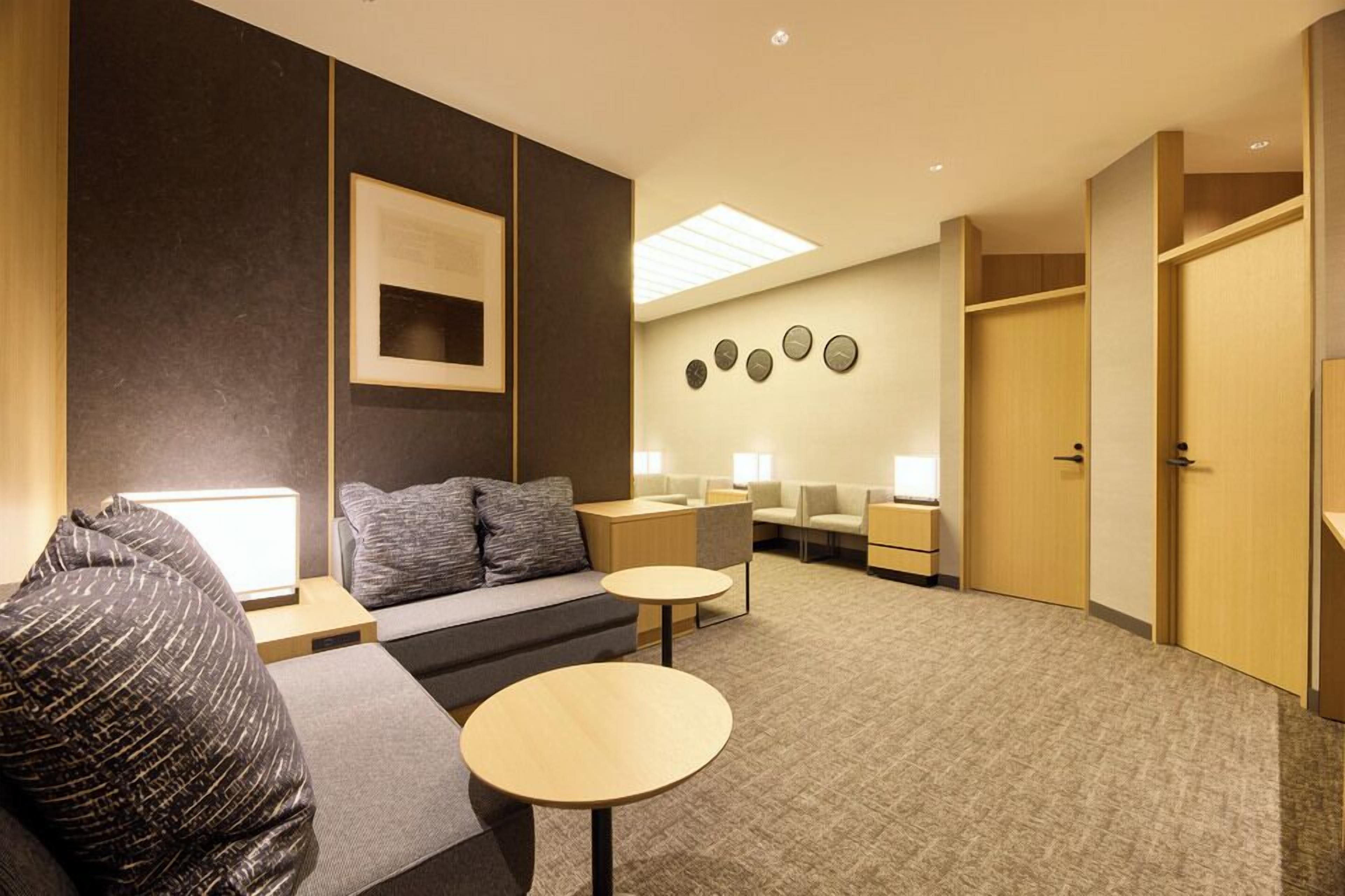 Ett modernt hotellrum med en soffa, två små bord, ett skrivbord och en väggklocka.