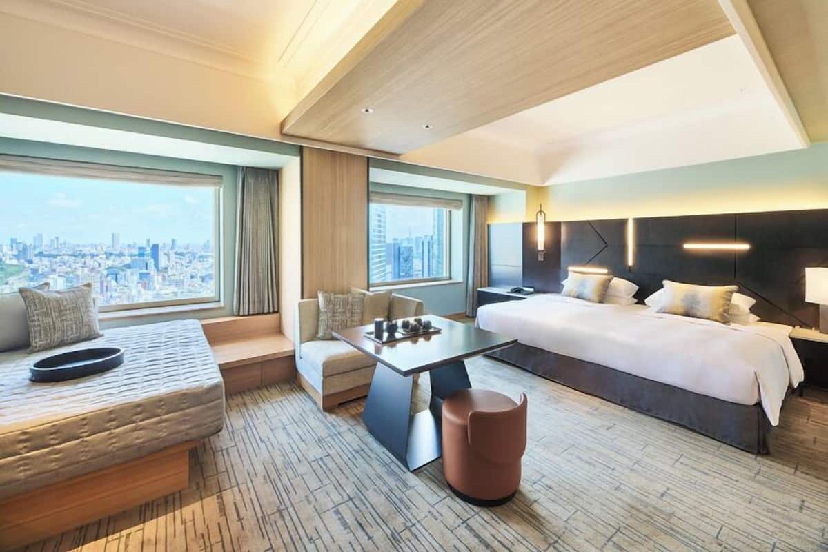 A modern hotel room with a large bed, a seating area with a table, and a view of the cityscape.