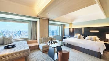 A modern hotel room with a large bed, a seating area with a table, and a view of the cityscape.