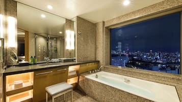 Un baño moderno con una bañera grande, un tocador con espejo y vistas a la ciudad a través de un amplio ventanal.