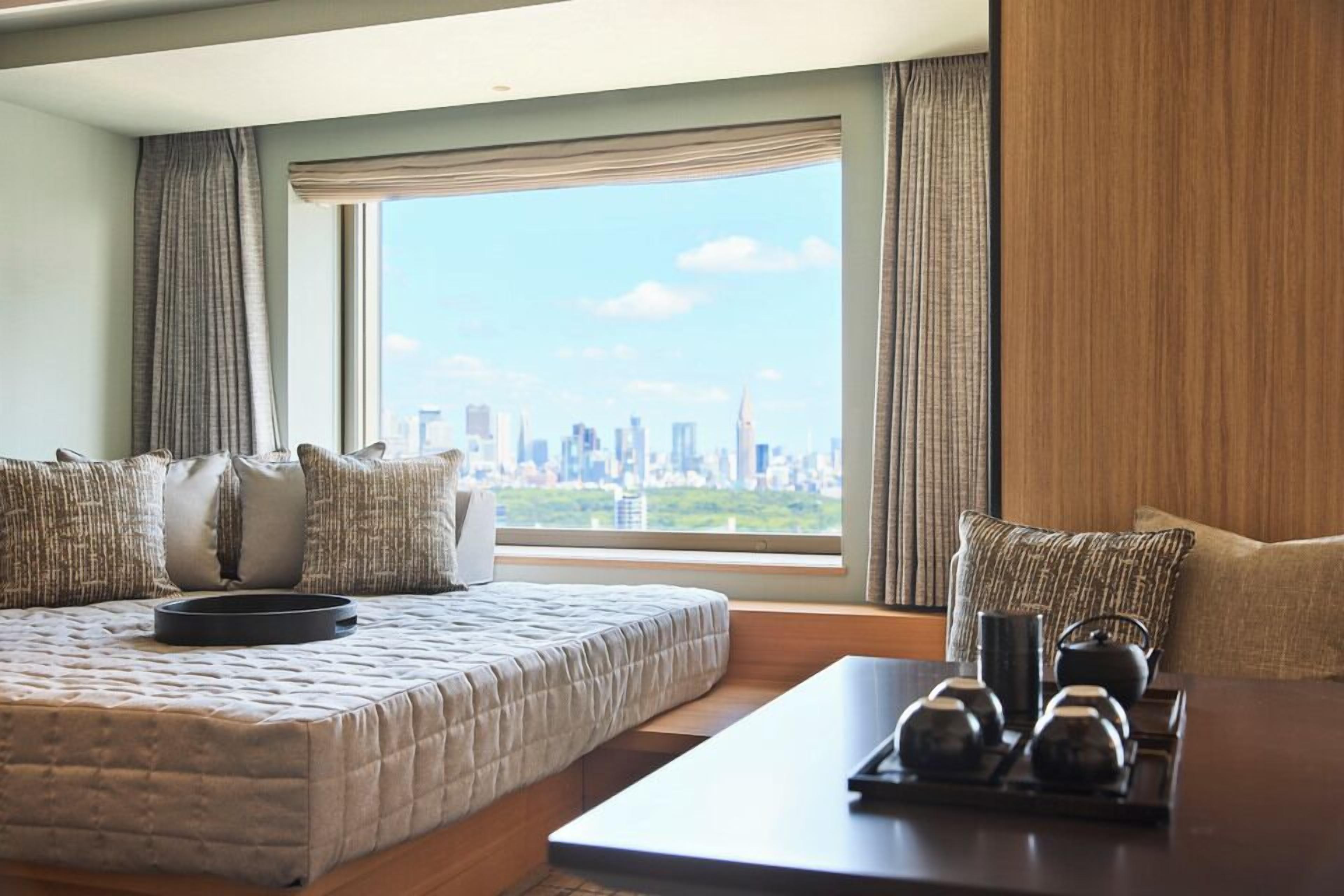 A hotel room with a bed, a table with teapots, and a view of a city skyline.
