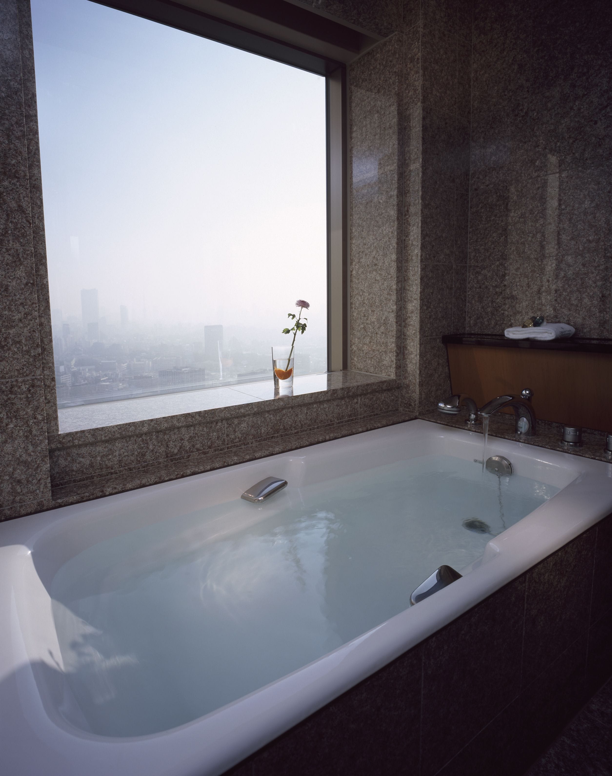 A modern bathroom with a large bathtub, a glass shower enclosure, and a view of a cityscape through a large window.