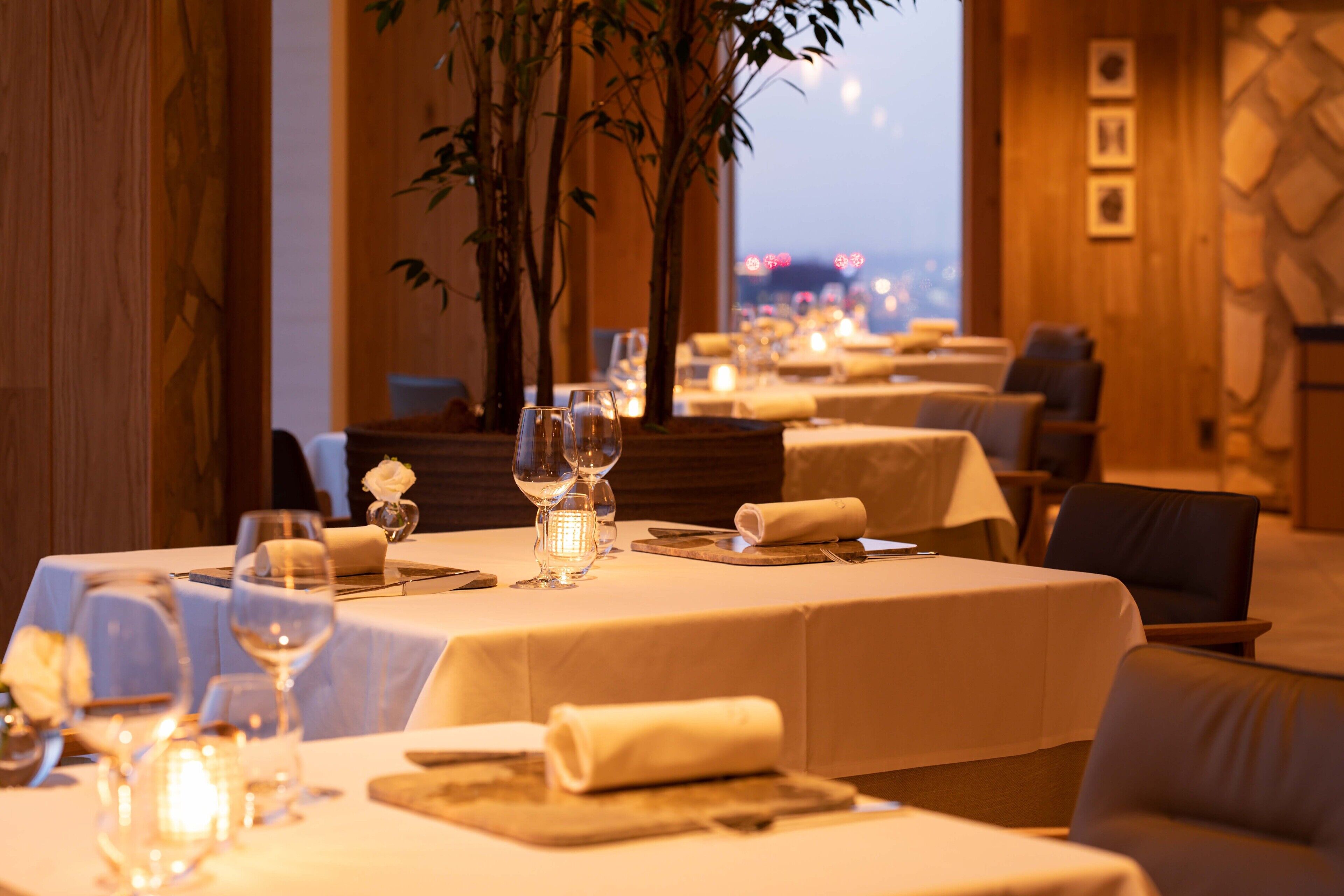 Een restaurant met gedekte tafels, kaarsen en uitzicht op de stadslijn.