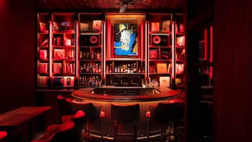 A bar area with a central counter, multiple shelves with bottles, and red upholstered chairs.