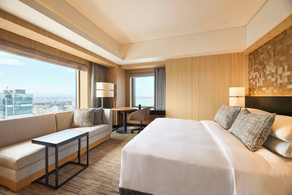 A hotel room with a large bed, a sofa, a small table, and a view of the city.