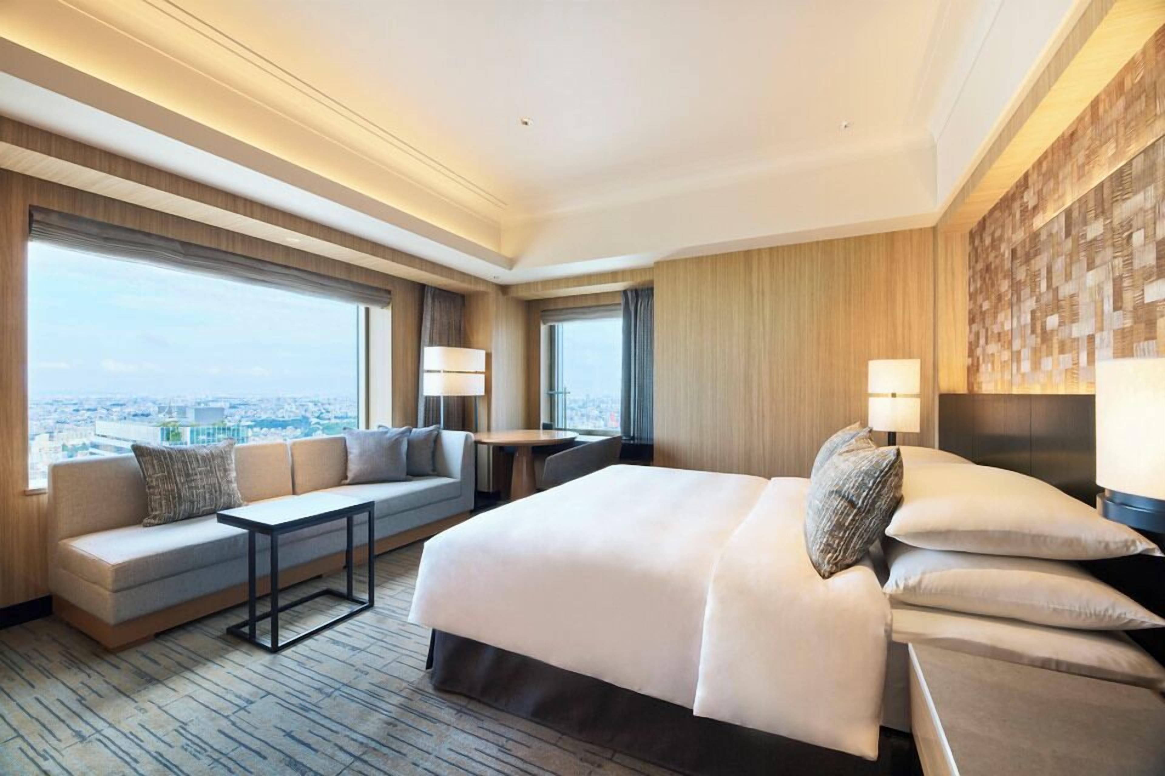 Een moderne hotelkamer met een groot bed, een bank, een tafeltje en uitzicht over de stad.