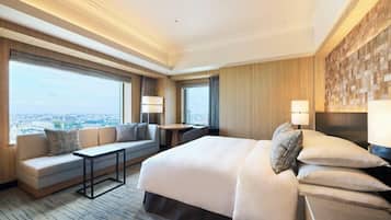 Een moderne hotelkamer met een groot bed, een bank, een tafeltje en uitzicht over de stad.