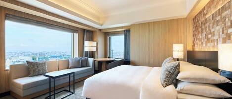 A modern hotel room with a large bed, a sofa, a small table, and a view of the city.
