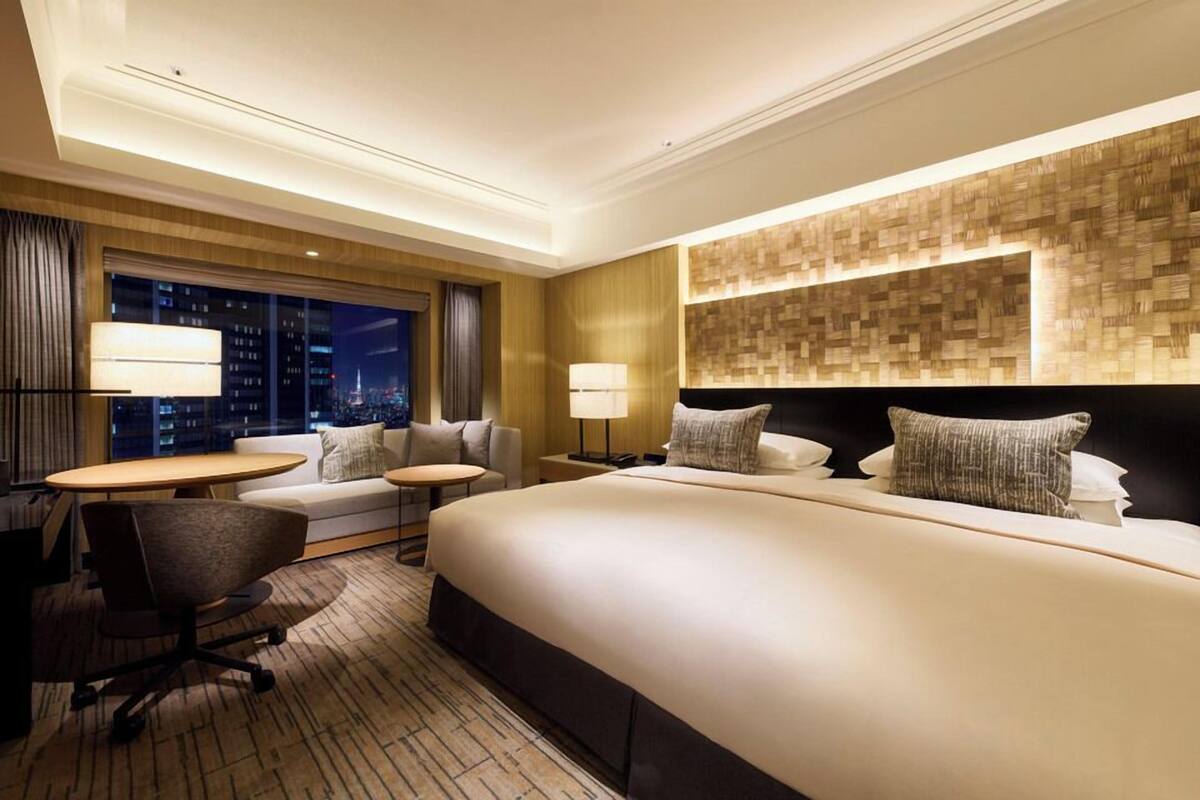 A hotel room with a large bed, two bedside tables, a desk with a chair, and a view of the city at night.