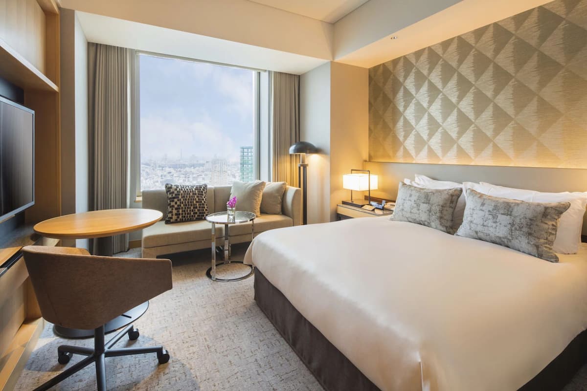 A hotel room with a large bed, a sofa, a small table, a desk, and a TV.