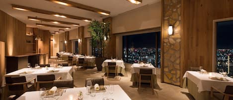 Un restaurant doté de nombreuses tables, aménagé pour accueillir les clients, et offrant une vue sur la ville grâce à de grandes fenêtres.