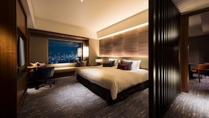 A modern hotel room with a large bed, a desk, and a view of the city at night.