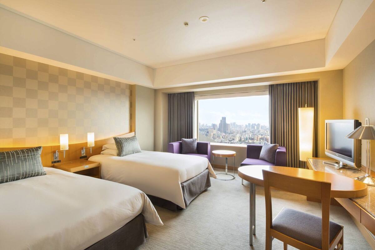 A hotel room with two beds, a sofa, a TV, and a city view.