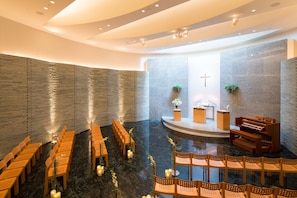 A church interior with pews arranged in rows, a piano, and a cross on the wall.