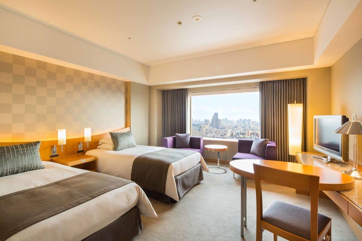 Habitación de hotel con dos camas, un sofá, un televisor y vistas a la ciudad.