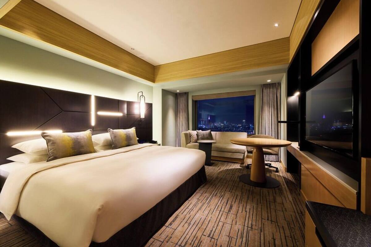A modern hotel room with a large bed, a seating area with a table, and a TV.