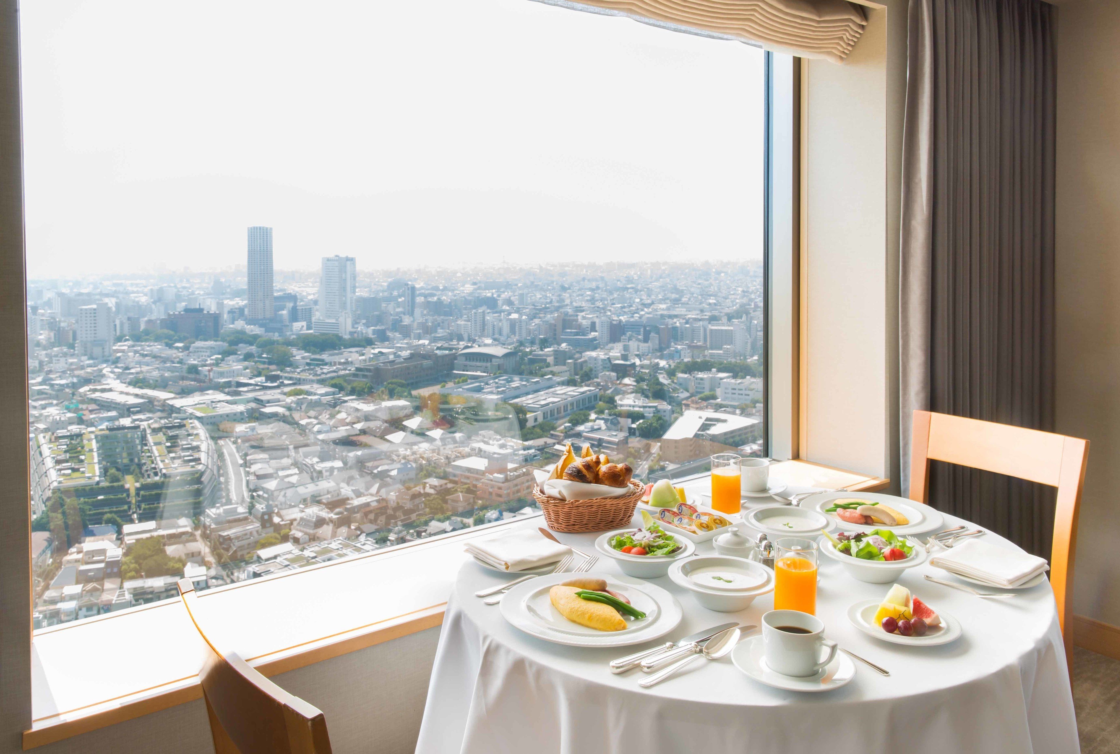 A dining table set with breakfast items and a city view through a large window.