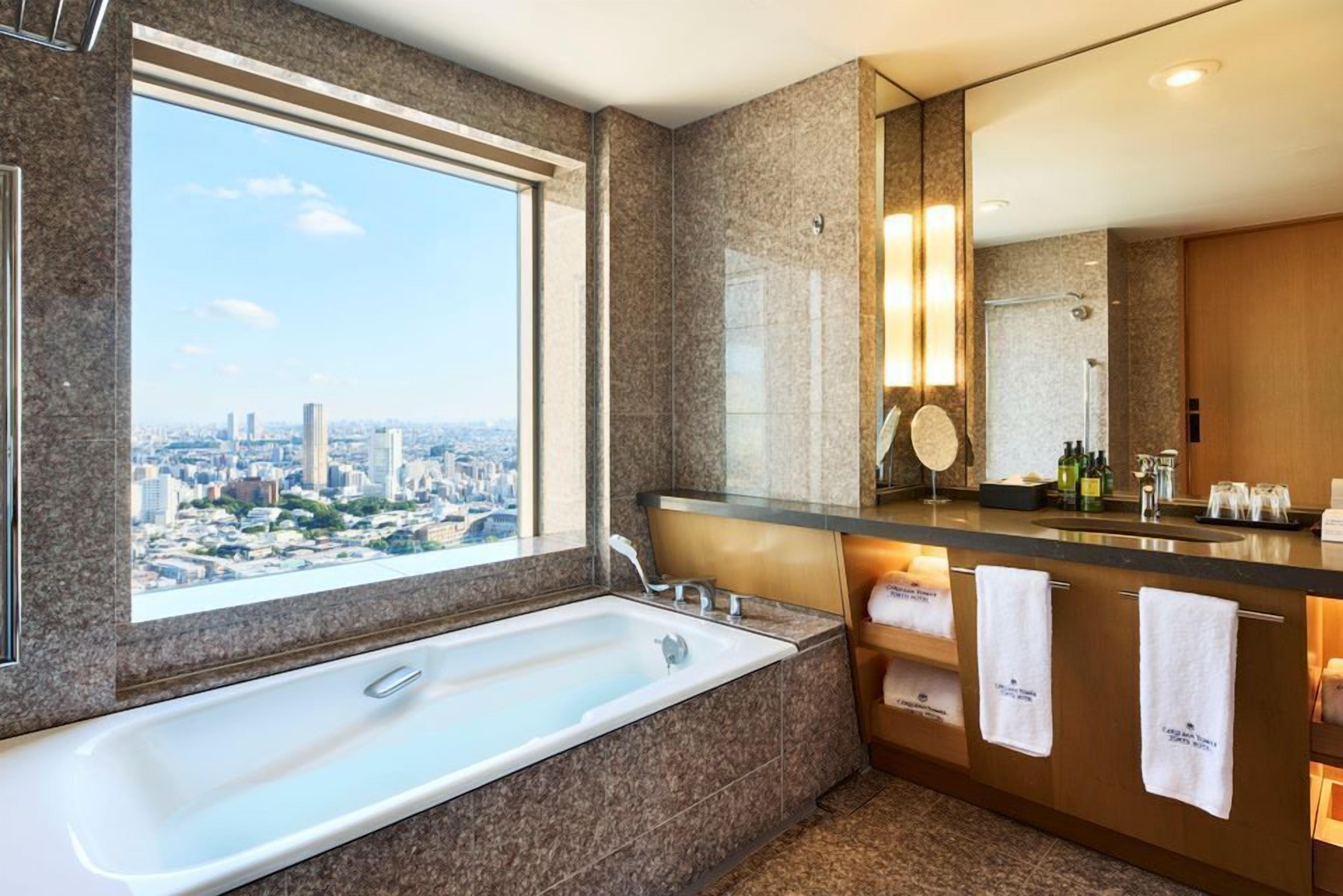 A modern bathroom with a large bathtub, a vanity with a mirror, and a view of the city.
