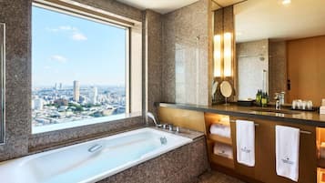A modern bathroom with a large bathtub, a vanity with a mirror, and a view of the city.